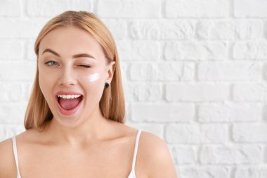 Beautiful young woman applying facial cream against white background