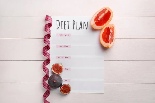 Sheet of paper with diet plan, measuring tape and fresh fruits on white wooden background — Stock Photo, Image