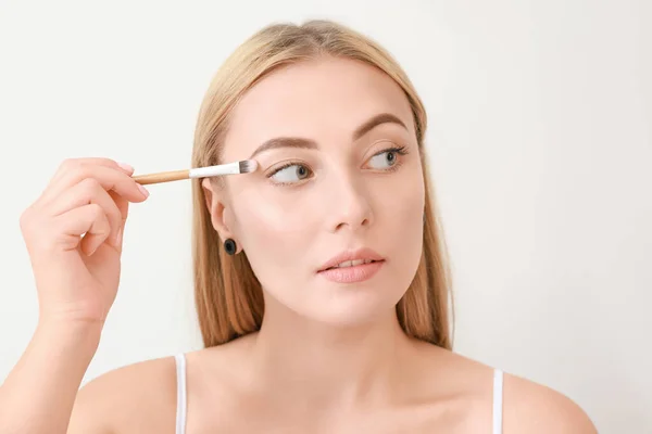 Beautiful young woman with makeup brush on light background — Stock Photo, Image