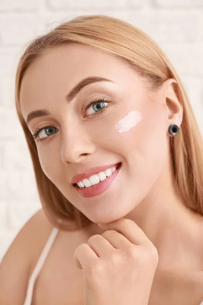 Hermosa mujer joven aplicando crema facial sobre fondo blanco — Foto de Stock