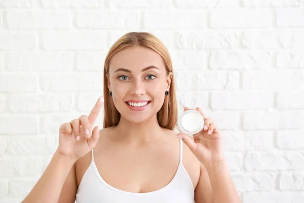 Hermosa mujer joven aplicando crema facial sobre fondo blanco — Foto de Stock