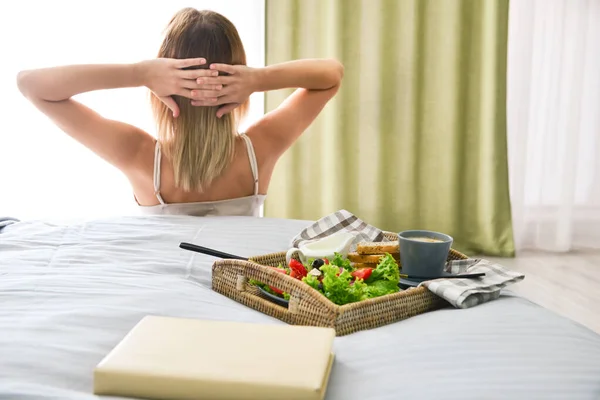 Tray with tasty breakfast on bed of young woman — Stock Photo, Image