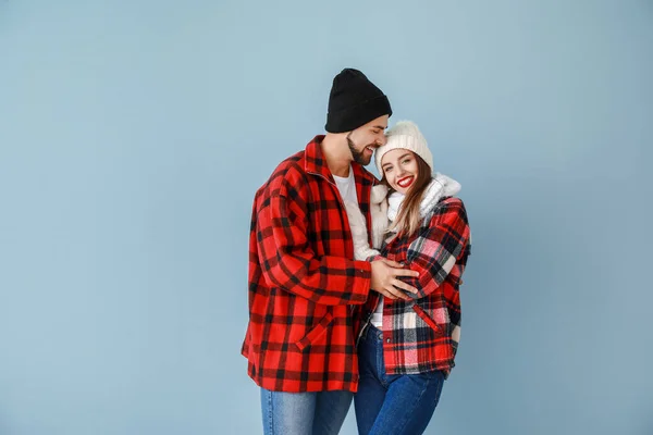 Happy young couple in warm winter clothes on color background — Stock Photo, Image