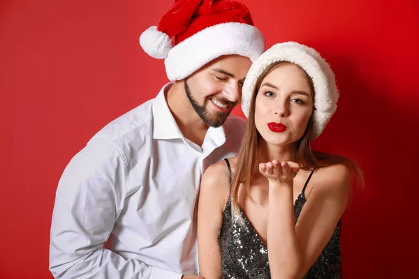 Glückliches junges Paar in Weihnachtsmützen auf farbigem Hintergrund — Stockfoto