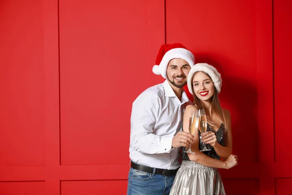 Happy young couple in Santa hats and with champagne on color background — Stock Photo, Image