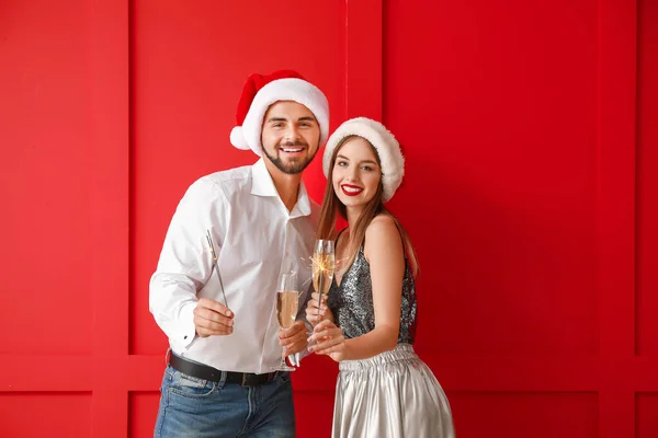 Szczęśliwa młoda para z Christmas sparklers i szampana na tle koloru — Zdjęcie stockowe