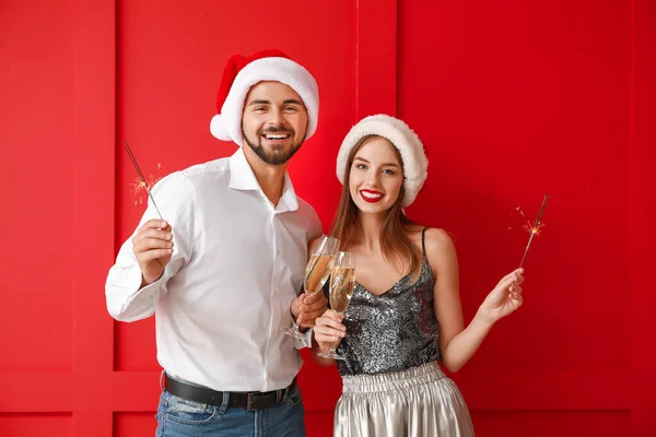 Jovem casal feliz com espumantes de Natal e champanhe no fundo de cor — Fotografia de Stock