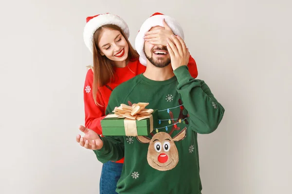 Happy young woman giving Christmas present to her boyfriend on light background — Stockfoto