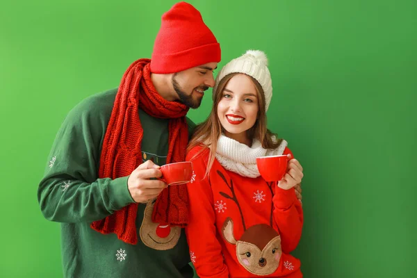 Jovem casal feliz em roupas de Natal e com chocolate quente no fundo de cor — Fotografia de Stock