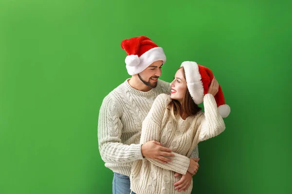 Feliz pareja joven en los sombreros de Santa sobre fondo de color — Foto de Stock