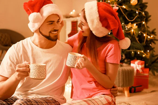 Feliz jovem casal beber chocolate quente enquanto celebra o Natal em casa — Fotografia de Stock