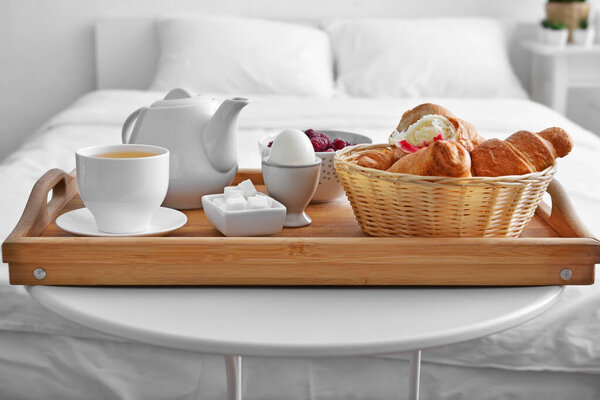 Tray with tasty breakfast on table in bedroom