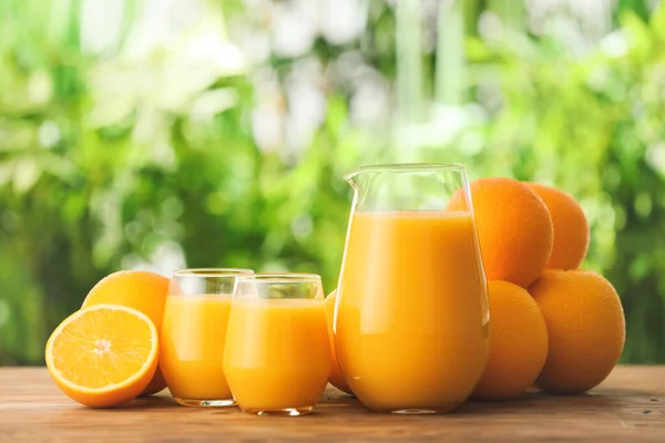 Γυαλιά με φρέσκο χυμό και πορτοκάλια στο τραπέζι σε εξωτερικούς χώρους — Φωτογραφία Αρχείου