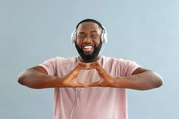 African-American man making heart with his hands while listening to music on color background — Stock Photo, Image