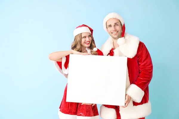 Young couple dressed as Santa Claus with blank poster on color background — Stock Photo, Image