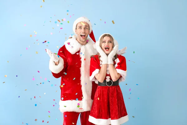 Pareja feliz vestida de Santa Claus con confeti volador sobre fondo de color — Foto de Stock