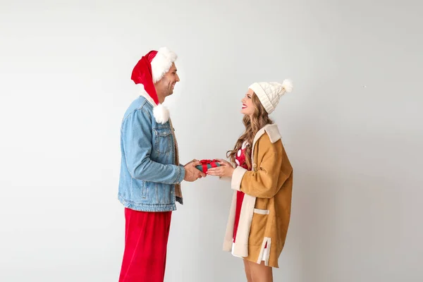 Young couple dressed as Santa Claus with Christmas gift on light background — Stock Photo, Image