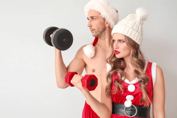 Young couple dressed as Santa Claus with dumbbells on light background — ストック写真