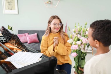 Küçük çocuk konserde piyano çaldıktan sonra genç bayana çiçek veriyor.