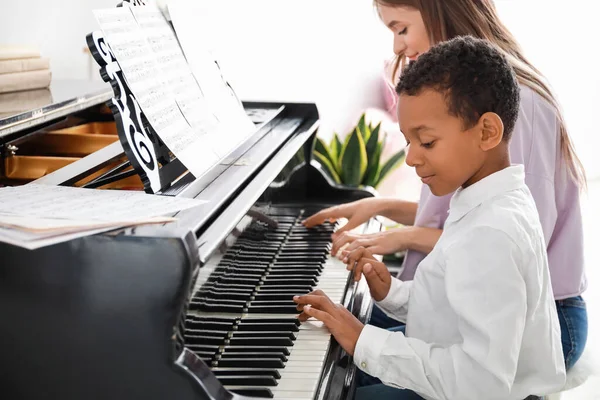 Vrouw onderwijs kleine Afro-Amerikaanse jongen om piano te spelen thuis — Stockfoto
