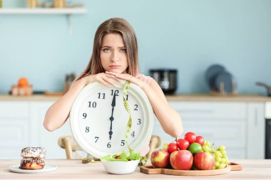 Mutfakta oturan saati ve yemeği olan üzgün bir kadın. Diyet kavramı