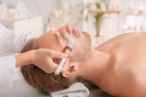 Kosmetikerin trägt Maske auf das Gesicht des Mannes im Wellness-Salon auf — Stockfoto