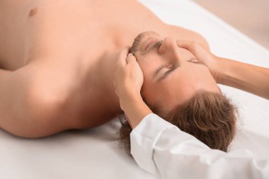 Genç adam spa salonunda yüz masajı yaptırıyor.