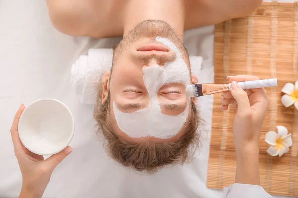 Cosmetologist applying mask onto man's face in spa salon — Stock Photo, Image