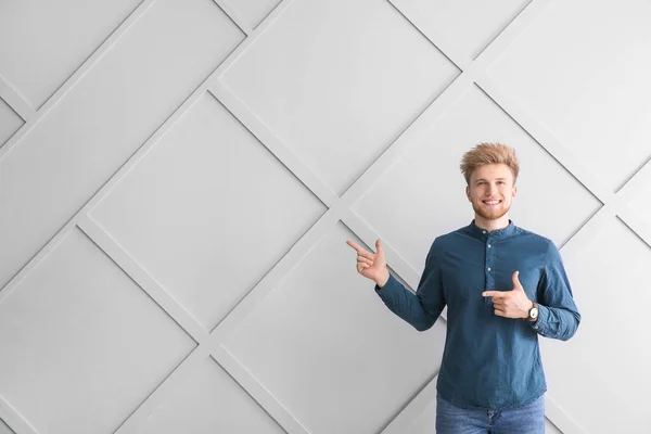 Portrait of young man pointing at something on grey background — Stock Photo, Image