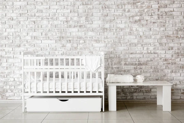 Κομψό κρεβάτι μωρού και τραπέζι κοντά σε τοίχο από τούβλα στο εσωτερικό του παιδικού δωματίου — Φωτογραφία Αρχείου