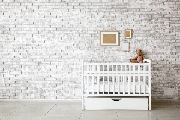 Elegante cama de bebé cerca de la pared de ladrillo en el interior de la habitación de los niños — Foto de Stock