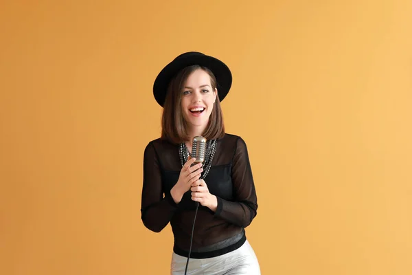 Schöne junge Sängerin mit Mikrofon auf farbigem Hintergrund — Stockfoto