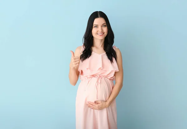 Hermosa joven embarazada mostrando el pulgar hacia arriba en el fondo de color — Foto de Stock