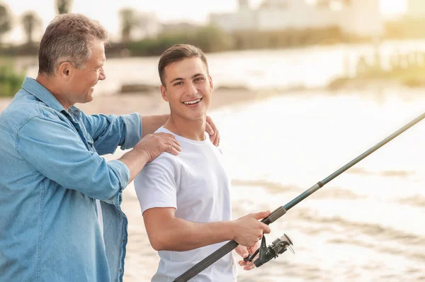 Молодий чоловік і його батько рибалять на річці — стокове фото