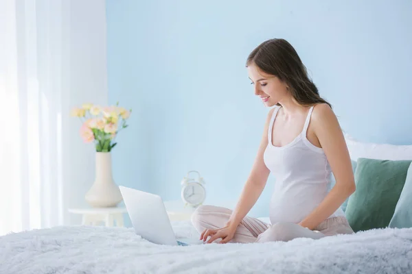 Beautiful pregnant woman with laptop sitting on bed — Stock Photo, Image