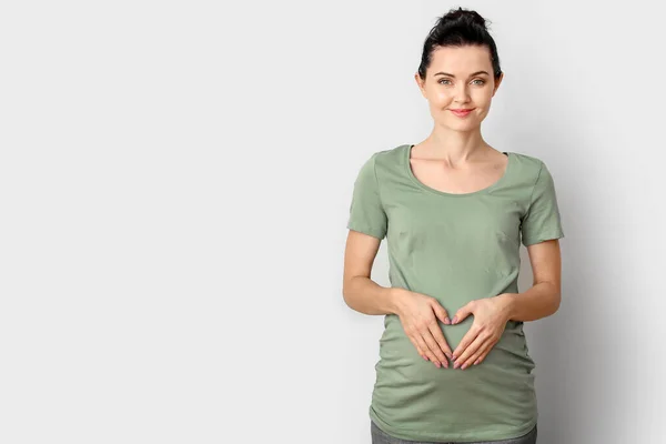 Schöne junge schwangere Frau auf hellem Hintergrund — Stockfoto