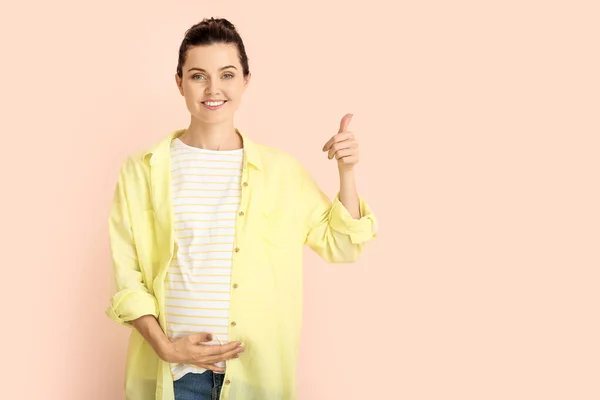 Hermosa joven embarazada mostrando el pulgar hacia arriba en el fondo de color — Foto de Stock