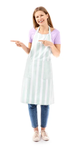 Beautiful young woman in apron pointing at something on white background — Stock Photo, Image