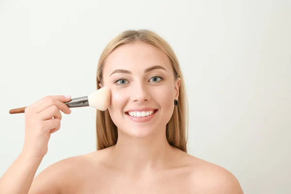 Hermosa mujer joven con cepillo de maquillaje sobre fondo claro — Foto de Stock