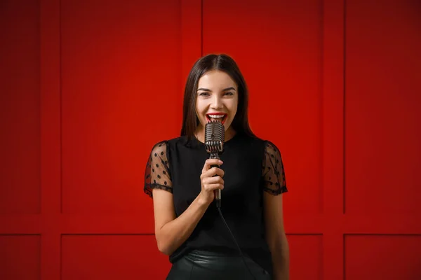 Hermosa joven cantante femenina con micrófono sobre fondo de color — Foto de Stock