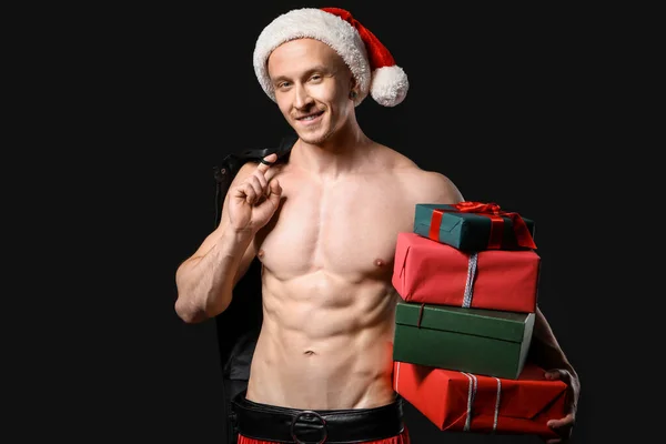 Young athletic Santa Claus with gifts on dark background — Stock Photo, Image