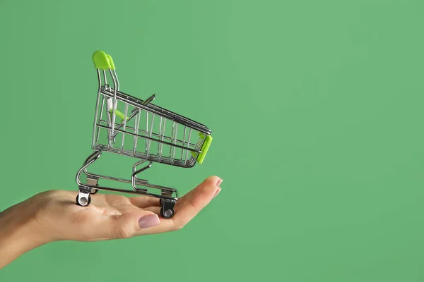 Mano femminile con vuoto piccolo carrello della spesa su sfondo a colori — Foto Stock