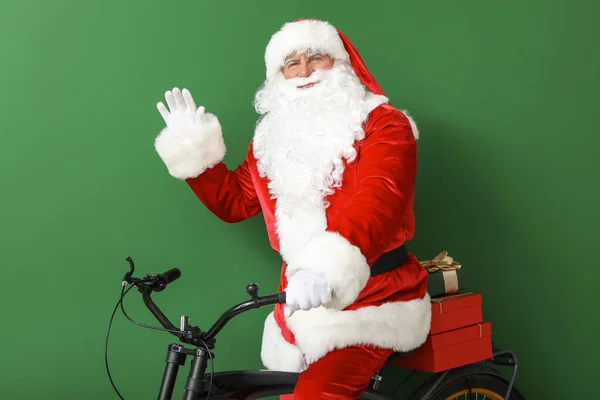 Santa Claus with Christmas gifts and bicycle on color background — Stock Photo, Image