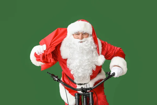 Santa Claus with bag riding bicycle on color background — Stock Photo, Image