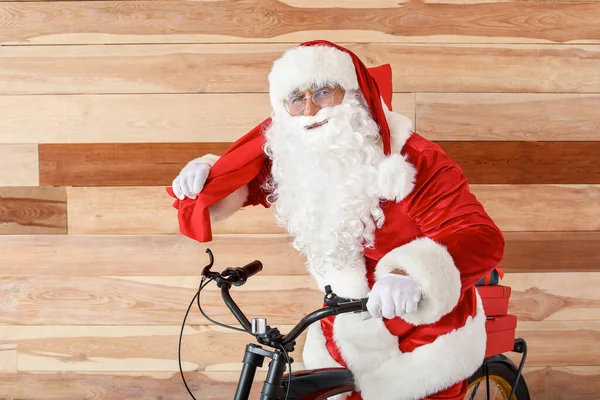 Święty Mikołaj z prezentów świątecznych i rowerów w pobliżu drewnianej ściany — Zdjęcie stockowe