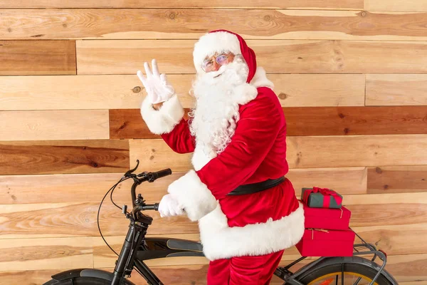 Święty Mikołaj z prezentami świątecznymi i rowerem pokazuje Ok gest na drewnianym tle — Zdjęcie stockowe