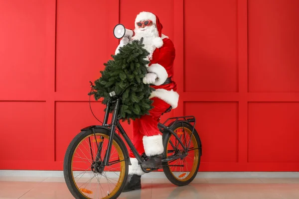 Санта Клаус з мегафоном, ялиновим деревом і велосипедом на кольоровому тлі. — стокове фото