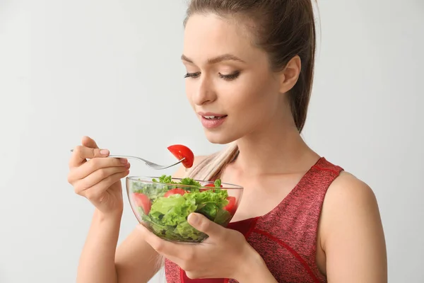 Спортивна жінка їсть здоровий овочевий салат на світлому фоні. Концепція дієти — стокове фото