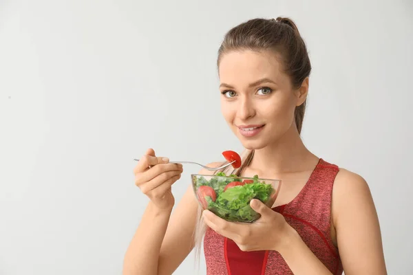 Sporty woman eating healthy vegetable salad on light background. Diet concept — Stock Photo, Image