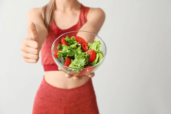 Sportig kvinna med hälsosam grönsakssallad visar tummen upp gest på ljus bakgrund, närbild. Diet koncept — Stockfoto